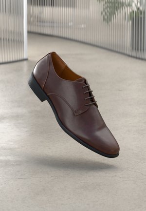 Chaussure habillée en cuir marron avec un bout rond, texture lisse et semelle en caoutchouc noir. Présente un design à lacets et des détails de couture minimalistes.