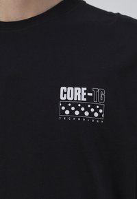 Camiseta de algodón negra con un estampado gráfico blanco que dice "TECNOLOGÍA CORE-TG" y un diseño de puntos. Cuello redondo clásico y mangas cortas.