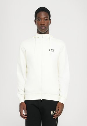 White zip-up hoodie made of soft fabric, featuring drawstrings and a logo on the chest. Smooth texture with a fitted design.