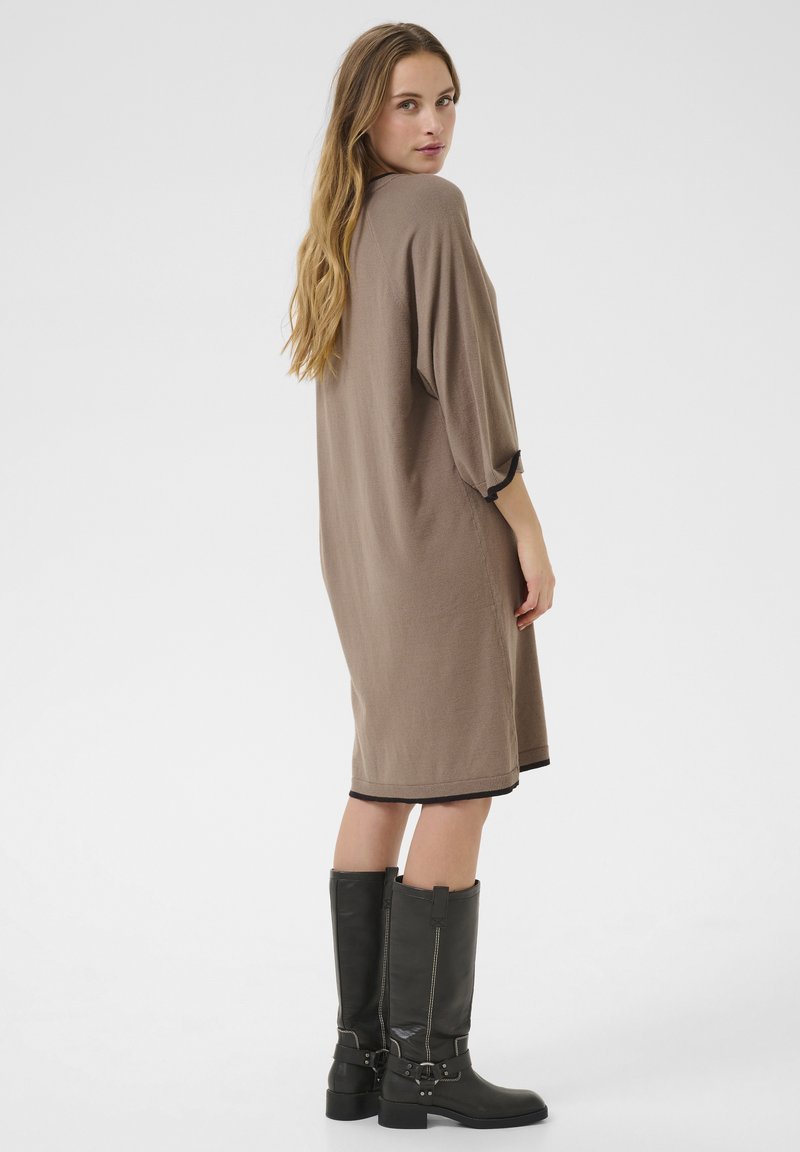 Braunes Strickkleid mit kurzen Ärmeln und abgerundetem Saum, kombiniert mit kniehohen schwarzen Stiefeln mit Schnallen und Steppnähten.