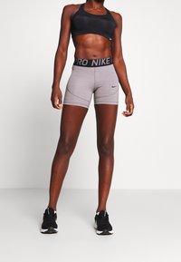 Svart sport-bh med nätdetaljer, kombinerad med grå, figurnära shorts med en svart midja märkt "PRO NIKE". Svarta träningsskor fulländar outfiten.