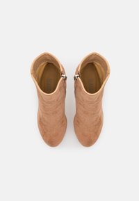 Bottines en daim beige clair avec une texture lisse, bout arrondi et fermeture éclair latérale. Accents matériels minimalistes à l'ouverture.