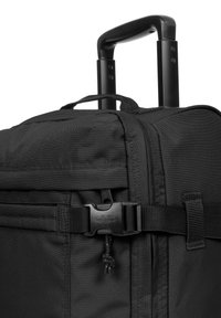 Borsa da viaggio nera con ruote, realizzata in tessuto testurizzato, manico regolabile, hardware resistente, cintura anteriore e manico laterale.