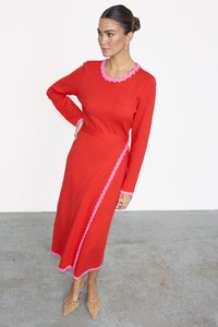 Rotes gestricktes Kleid mit langen Ärmeln und tailliertem Schnitt. Verfügt über pinkfarbene Rüschendetails am Ausschnitt und an einer Seite. Bis zur Mitte der Waden.