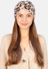 Bandeau en tissu doux et texturé avec un imprimé léopard, doté d'un design à l'avant torsadé. Palette de couleurs neutres comprenant du beige, du noir et du brun.