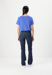 T-shirt en coton bleu et jeans évasés en denim foncé, avec une taille mi-haute, une texture lisse et des poches arrière, associés à des chaussures blanches.