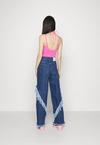 Růžová tank top bez zad s vysokým pasem jeansy z denimu, které mají světlé modré třásně na nohavicích, a růžové platformové boty.