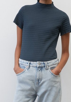 Mörkblå texturerad kortärmad topp med hög krage, kombinerad med ljusblå denimjeans. Skjortan har subtila ribbningar och mjukt tyg.