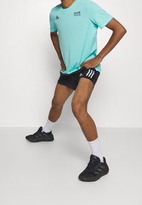 Světle modré sportovní tričko s černým logem, spárované s černými šortkami s bílými pruhy, bílými ponožkami a černými běžeckými botami.