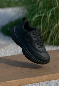 Svarte sportssko med en glatt lær overdel, polstret krage, tykk gummisåle og teksturerte detaljer. Lett design med snøring.