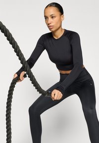 Black long-sleeve athletic top and leggings, fitted design, smooth texture. Person gripping a textured exercise rope.