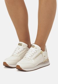 Zapatillas de piel blanca con acentos dorados, textura perforada, un zipper lateral y suela de goma, con puntera redondeada y sistema de cordones.