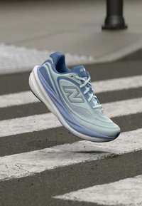 Ανοιχτό μπλε και ναυτικό αθλητικό παπούτσι με λευκή σόλα που αιωρείται πάνω από μια διάβαση πεζών σε ασφαλτοστρωμένο δρόμο.