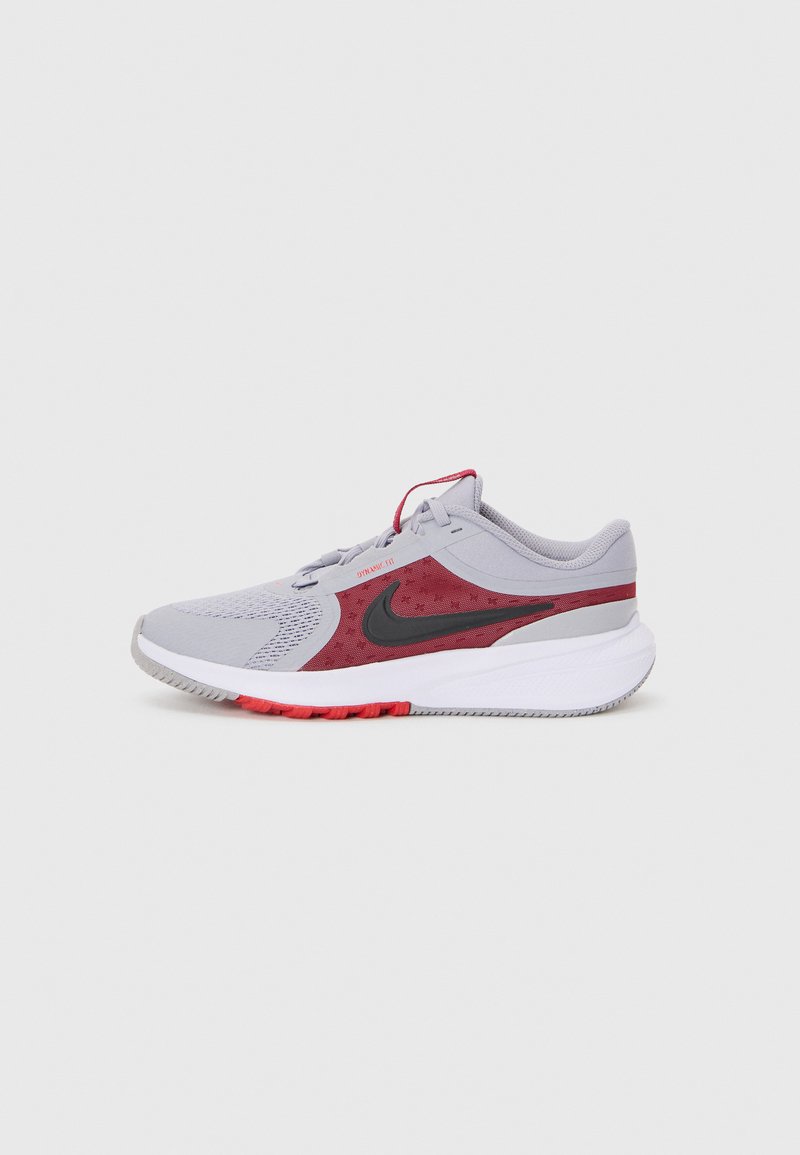 Zapatilla deportiva gris con acentos rojos, parte superior de malla, collar acolchado, detalle del logo en negro y suela de goma texturizada para agarre.