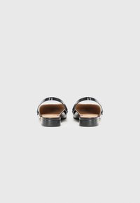 Black patent leather sandals with a flat heel, open back, and contrasting tan insole. Features simple design and adjustable strap detail.