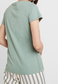 Myntgrön kortärmad T-shirt, tillverkad av mjuk bomull. Har rund halslinning och sidslitsar i fållen för ökad rörelsefrihet.