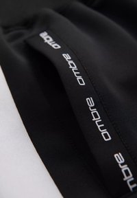 Zwarte sportshorts met witte tekstbranding langs de tailleband, voorzien van een gladde stofafwerking en een elastische taille voor flexibele pasvorm.