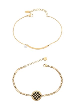 Dwie złote bransoletki na łańcuszku: jedna z zakrzywionym paskiem i małym przezroczystym zawieszkiem, druga z okrągłym, czarno-złotym centrum w kratkę.