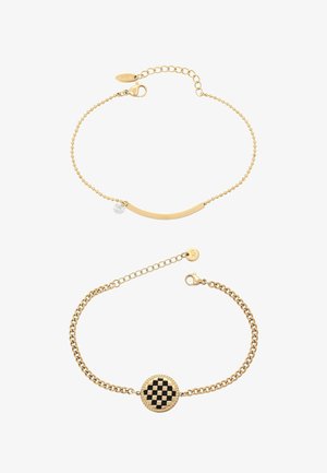 Dwie złote bransoletki na łańcuszku: jedna z zakrzywionym paskiem i małym przezroczystym zawieszkiem, druga z okrągłym, czarno-złotym centrum w kratkę.