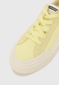 Scarpa da ginnastica in tela gialla con lacci piatti, suola in gomma e dettagli cuciti. Punta arrotondata e tessuto strutturato per un look casual.