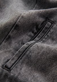 Close-up af sort denimstof, der viser en syet forlommer med synlig diagonalt vævet tekstur og skyggefulde folder.