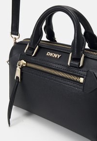 Borsa a mano in pelle nera con hardware dorato, scomparti con zip e manici superiori. Presenta una tracolla removibile e un marchio in rilievo.