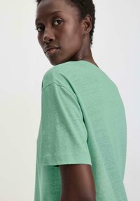 Mintgroene t-shirt met korte mouwen en een brede halslijn, gemaakt van een zachte stof. Het shirt heeft een ontspannen pasvorm en standaard stikdetails.