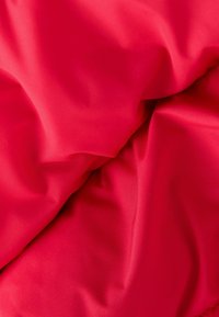 Tela roja con una textura suave, que presenta pliegues y arrugas suaves, reflejando la luz de manera sutil. No hay patrones o elementos metálicos visibles.