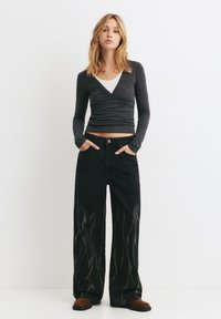 Sorte bredbenede jeans med flamme mønstre, parret med en langærmet grå top med V-udskæring og en hvid tanktop under.