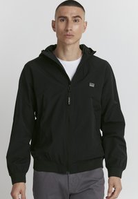 Black hooded bomber jacket with a zip front, fitted cuffs, and hem; smooth texture; small logo patch on the left chest.