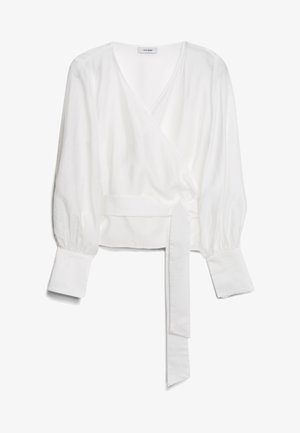 Blouse blanche à manches longues, enroulée, avec un décolleté en V profond, des poignets larges et une ceinture en tissu nouée à la taille, reposant à plat sur un fond blanc.