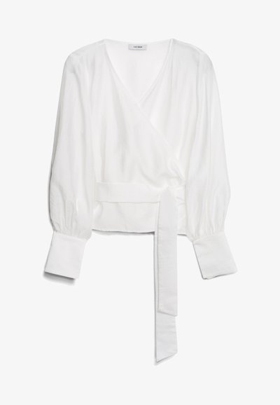 Blusa branca de mangas longas com decote em V profundo, punhos largos e faixa de tecido na cintura, deitada sobre um fundo branco.