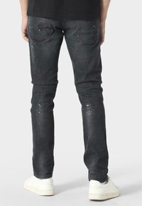 Černé džíny s slim fit střihem, které mají jemné bílé skvrny od barvy a zadní kapsy. V kombinaci s bílými teniskami.