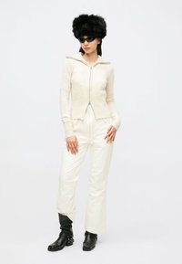 Hvit ribbestrikket genser med glidelås, kremfargede bukser og svart hatt i imitasjonspels. Stilrene svarte støvler med spenner fullfører antrekket.