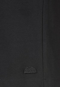 Tessuto nero con una superficie texturizzata, che presenta un piccolo logo ricamato nero a forma semicerchio nella parte inferiore.