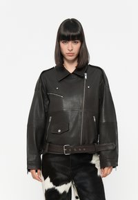 Black leather jacket with oversized fit, large collar, multiple zippered pockets, and a cinched belt. Smooth texture and shiny finish.