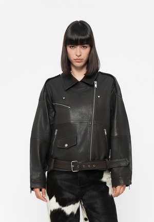 Black leather jacket with oversized fit, large collar, multiple zippered pockets, and a cinched belt. Smooth texture and shiny finish.
