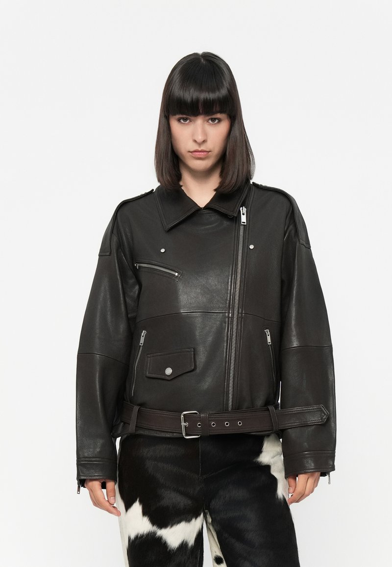 Black leather jacket with oversized fit, large collar, multiple zippered pockets, and a cinched belt. Smooth texture and shiny finish.