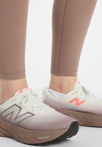 Hellrosa sportliche Leggings kombiniert mit weißen New Balance Schuhen, die hellrosa und braune Akzente, eine strukturierte Mesh-Oberfläche und eine schwarze Sohle aufweisen.