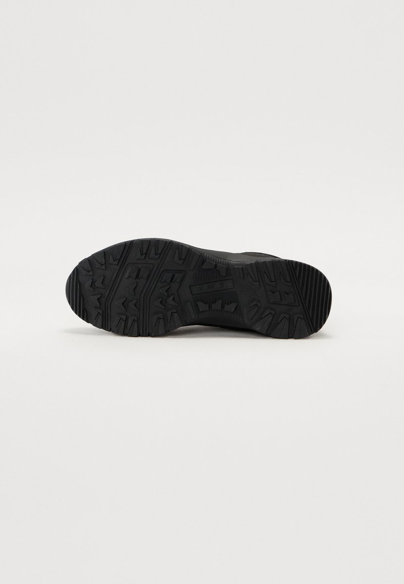Schwarze Sportschuhsohle mit robustem Profil, strukturiertem Gummimaterial und ausgeprägten Stollen für Grip und Traktion.