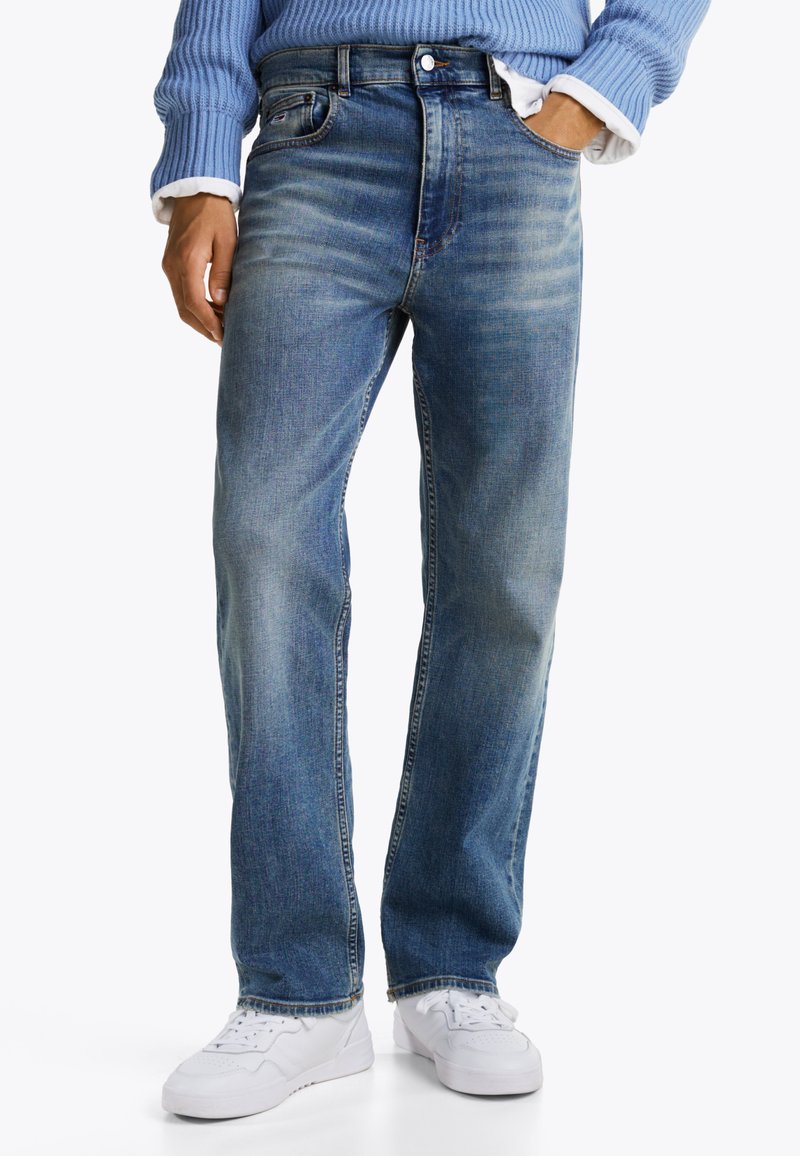Vaqueros de denim azul claro con un diseño de pierna recta, ligero desgaste y estilo tradicional de cinco bolsillos. Combinados con zapatillas blancas.