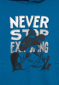 Blue hoodie featuring a graphic design with the phrase "NEVER STOP EXPLORING" and an illustration of a bear snowboarding with ski equipment.