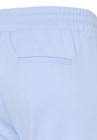Light blue pants with elastic waistband and a horizontal slit back pocket, shown from the rear close-up.