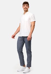 Camisa de lino blanca de manga corta con un bolsillo en el pecho, combinada con pantalones texturizados gris oscuro y zapatillas blancas. Diseño simple y casual.