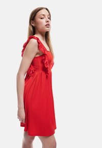 Rotes Kleid mit Rüscheträgern, tailliertem Oberteil und schwingendem Rock; strukturierter Stoff mit einem subtilen Muster. Seitenansicht, die die Designdetails zeigt.