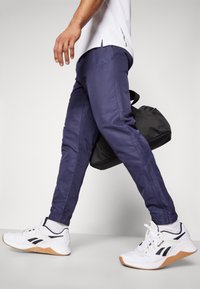 Pantalons de sport bleu marine avec des poignets élastiques et des panneaux latéraux, associés à des baskets blanches avec des accents noirs et une semelle en caoutchouc.