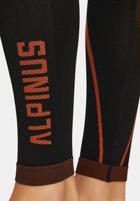 Czarne legginsy z pionowym napisem "ALPINUS" w teksturowanym pomarańczowym kolorze. Oferują kontrastowe pomarańczowe szwy wzdłuż szwów oraz wzorzysty pas.