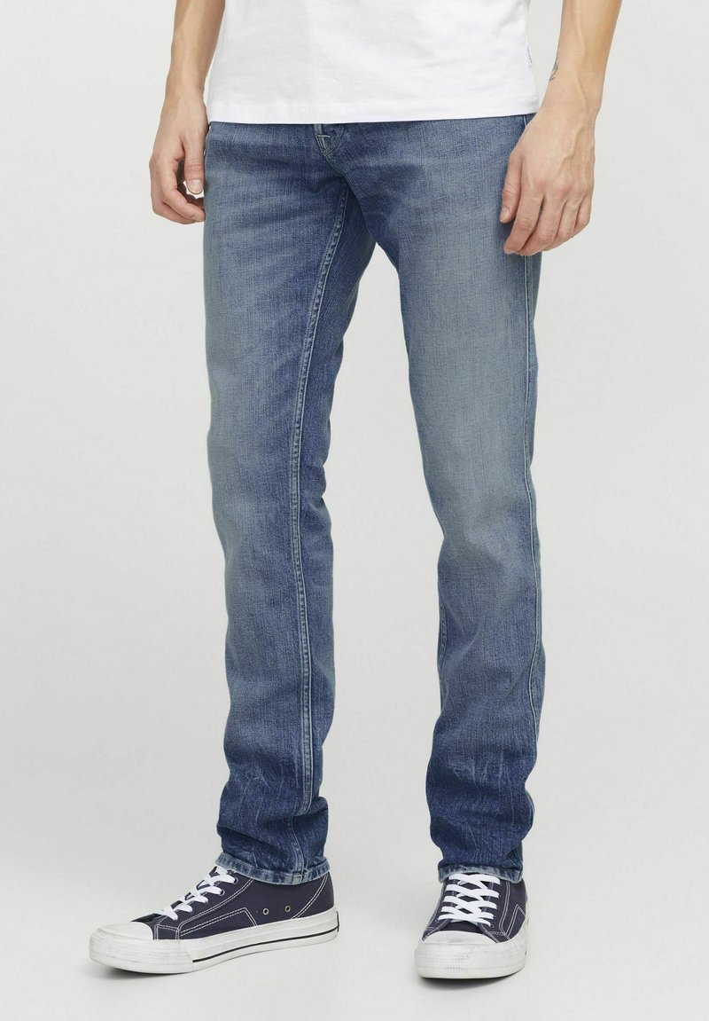 Jeans en denim dans un lavage bleu clair, présentant une coupe slim, une texture délavée et un design à cinq poches. Assortis avec des baskets foncées.