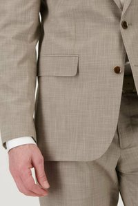 Lichtbeige colbert, textuurstof, enkele knoopsluiting, zijkwast, met een witte hemdmanchet zichtbaar. Getailleerde pasvorm, strakke lijnen.
