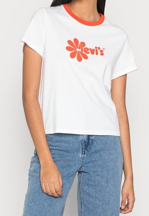 Hvid bomuld T-shirt med orange ribbet halsudskæring og stort rødt blomsterlogo. Kortærmet og kort design kombineret med blå denimjeans.